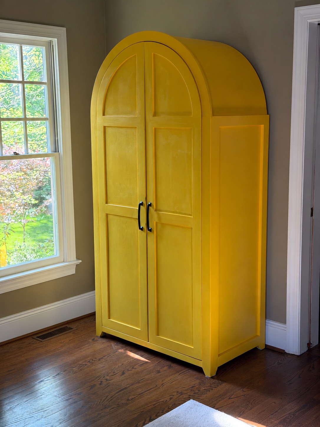 Completed bright yellow playroom armoire with an arched top, paneled double doors, and black handles
