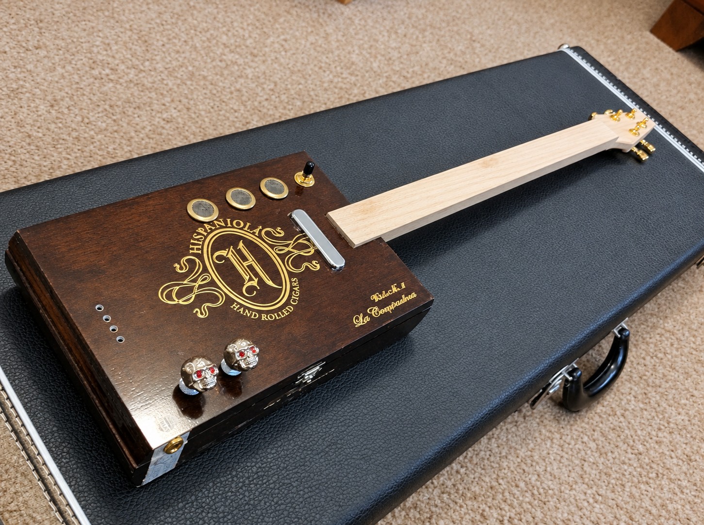 Cigar box guitar in assembly with screened sound holes, skull knobs and an unstrung neck