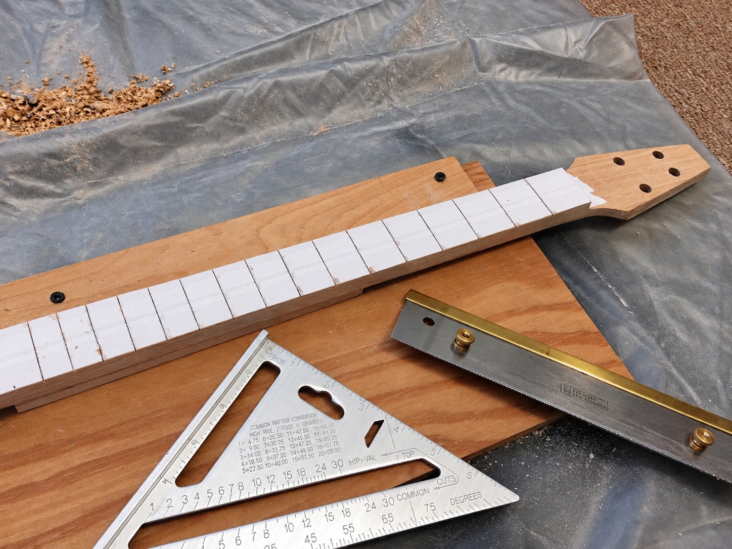 Paper fret-position template on the wooden neck beside a saw and square