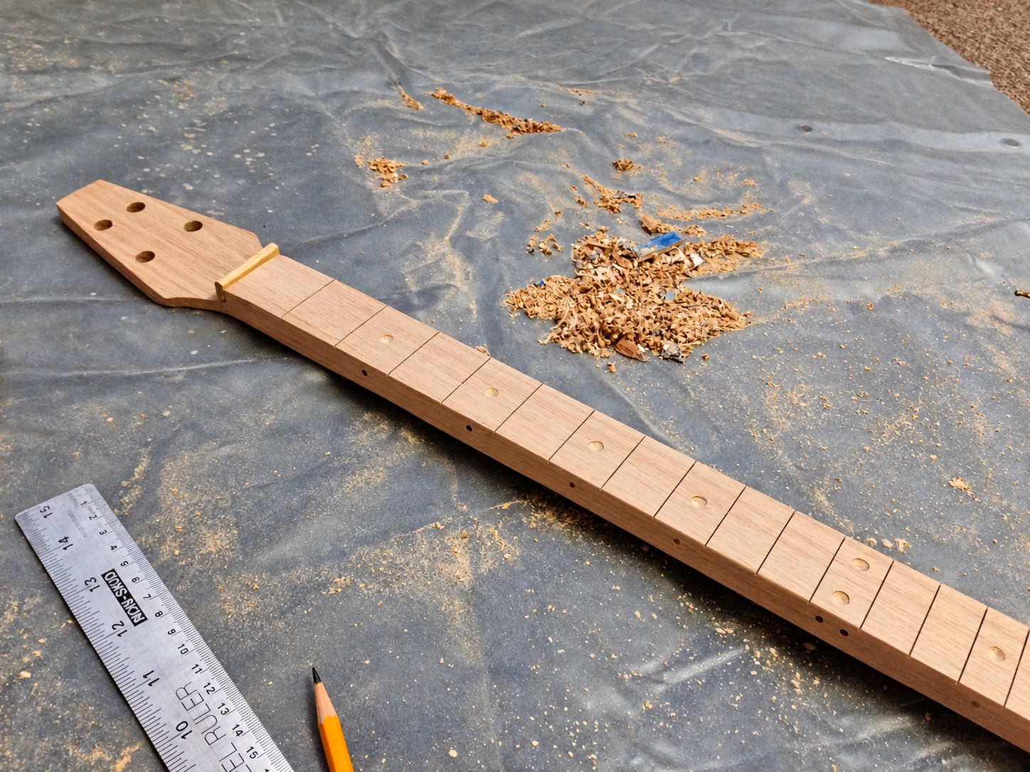 Wooden neck with fret slots, marker holes and a nut beside wood shavings