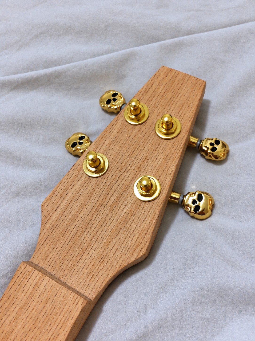 Four gold skull-shaped tuner buttons on the wooden headstock